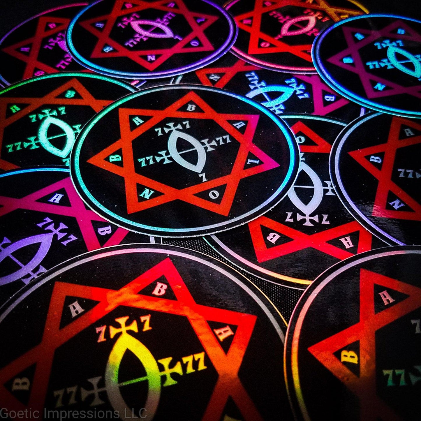 A pile of three inch circular holographic stickers. The stickers have a black background and a white and red symbol featuring the Star of Babalon. The holographic paper shines in a wide arrange of rainbow colors when the light catches it at different angles.