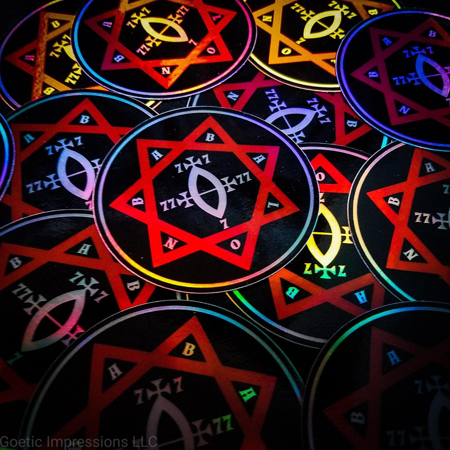 A pile of three inch circular holographic stickers. The stickers have a black background and a white and red symbol featuring the Star of Babalon. The holographic paper shines in a wide arrange of rainbow colors when the light catches it at different angles.