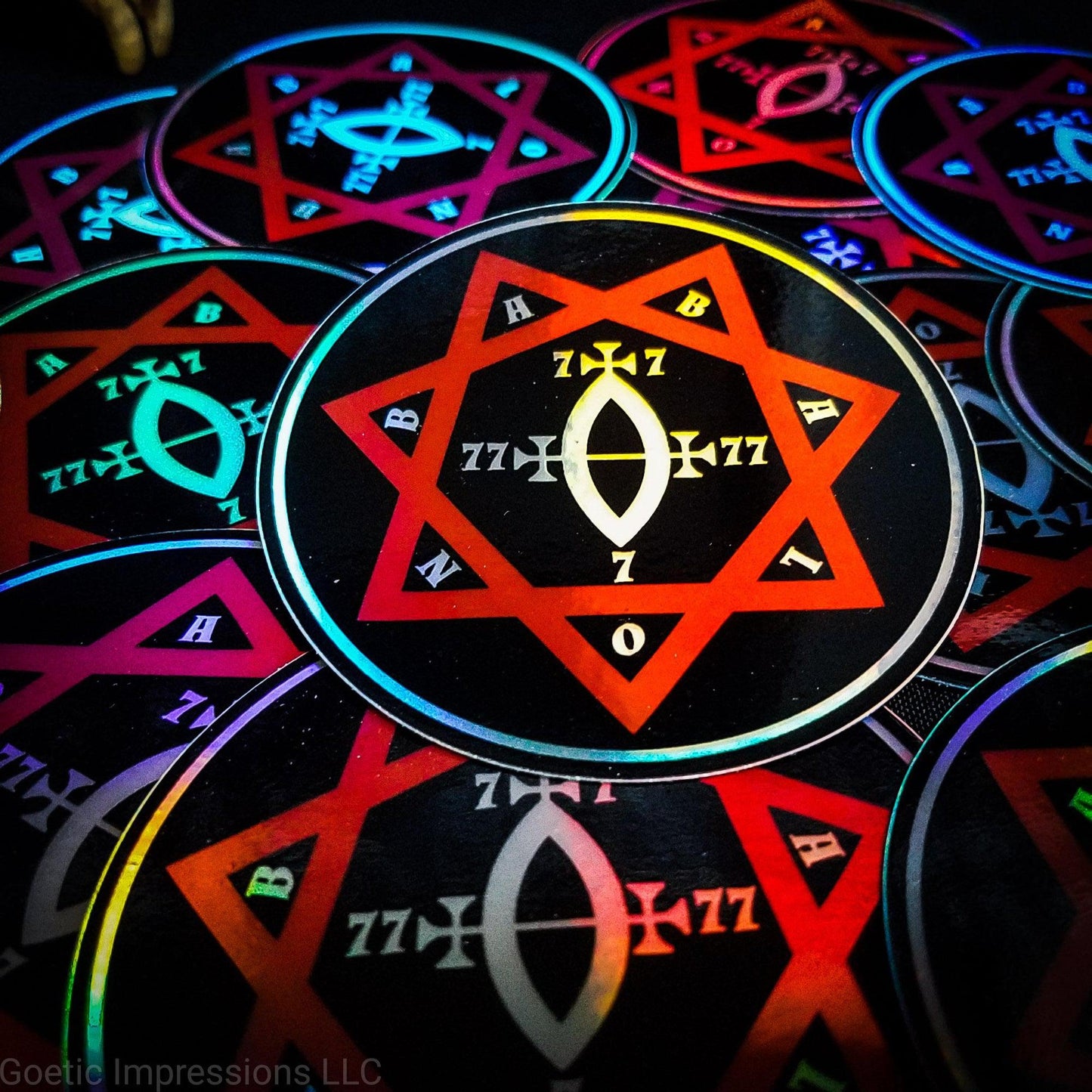 A pile of three inch circular holographic stickers. The stickers have a black background and a white and red symbol featuring the Star of Babalon. The holographic paper shines in a wide arrange of rainbow colors when the light catches it at different angles.