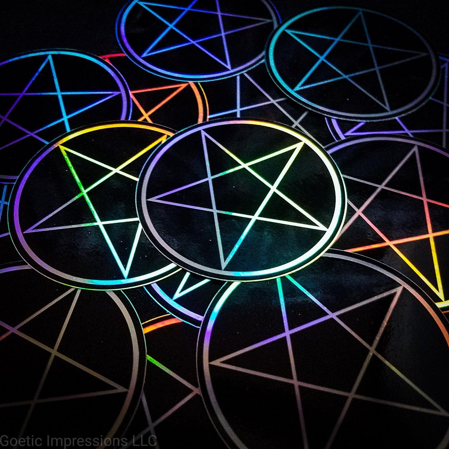 A pile of three inch circular holographic stickers. The stickers have a black background and a white symbol featuring the a traditional pentacle. The holographic paper shines in a wide arrange of rainbow colors when the light catches it at different angles.