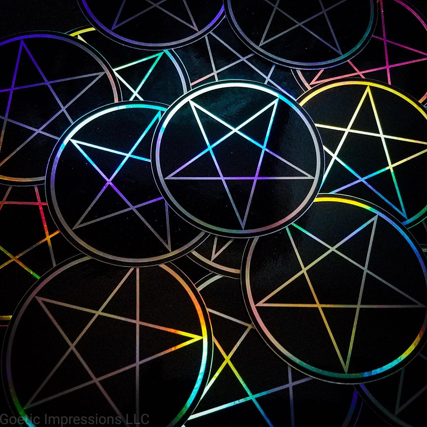 A pile of three inch circular holographic stickers. The stickers have a black background and a white symbol featuring the a traditional pentacle. The holographic paper shines in a wide arrange of rainbow colors when the light catches it at different angles.