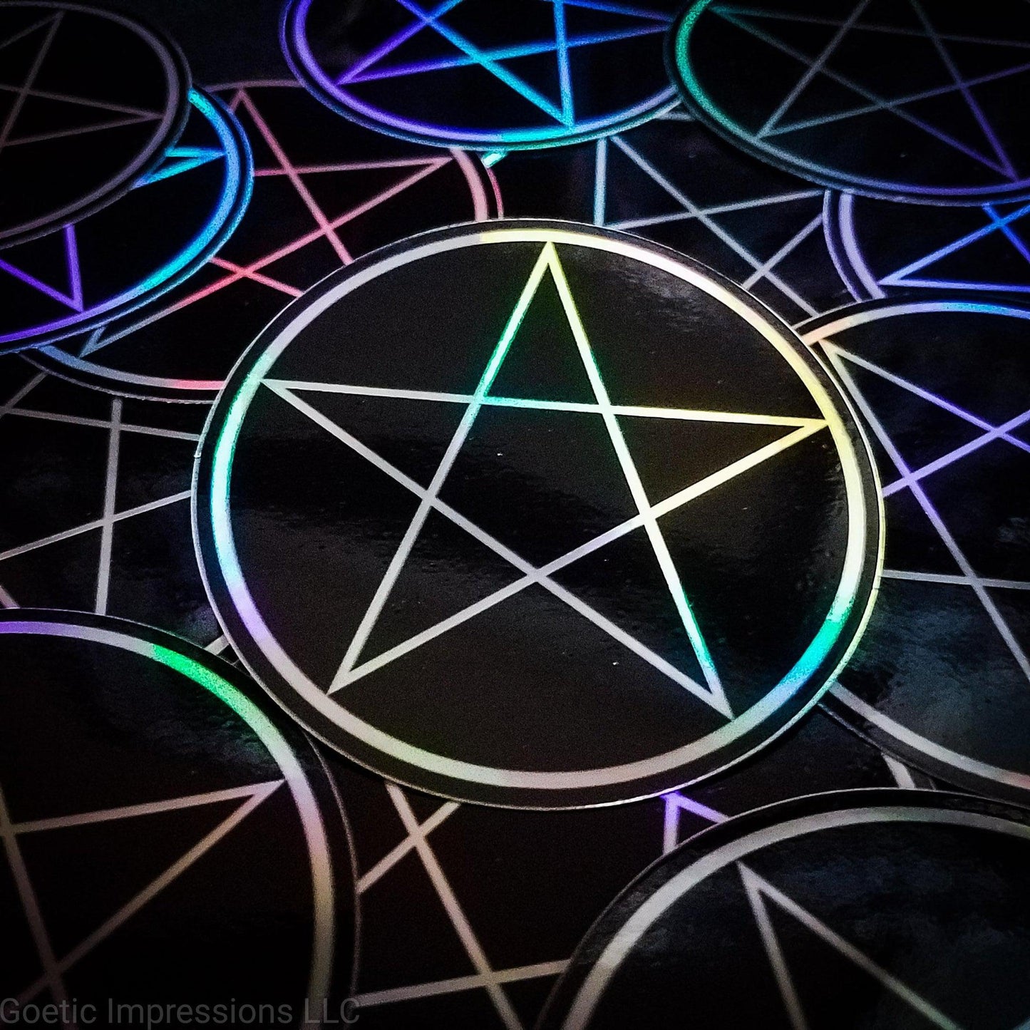 A pile of three inch circular holographic stickers. The stickers have a black background and a white symbol featuring the a traditional pentacle. The holographic paper shines in a wide arrange of rainbow colors when the light catches it at different angles.