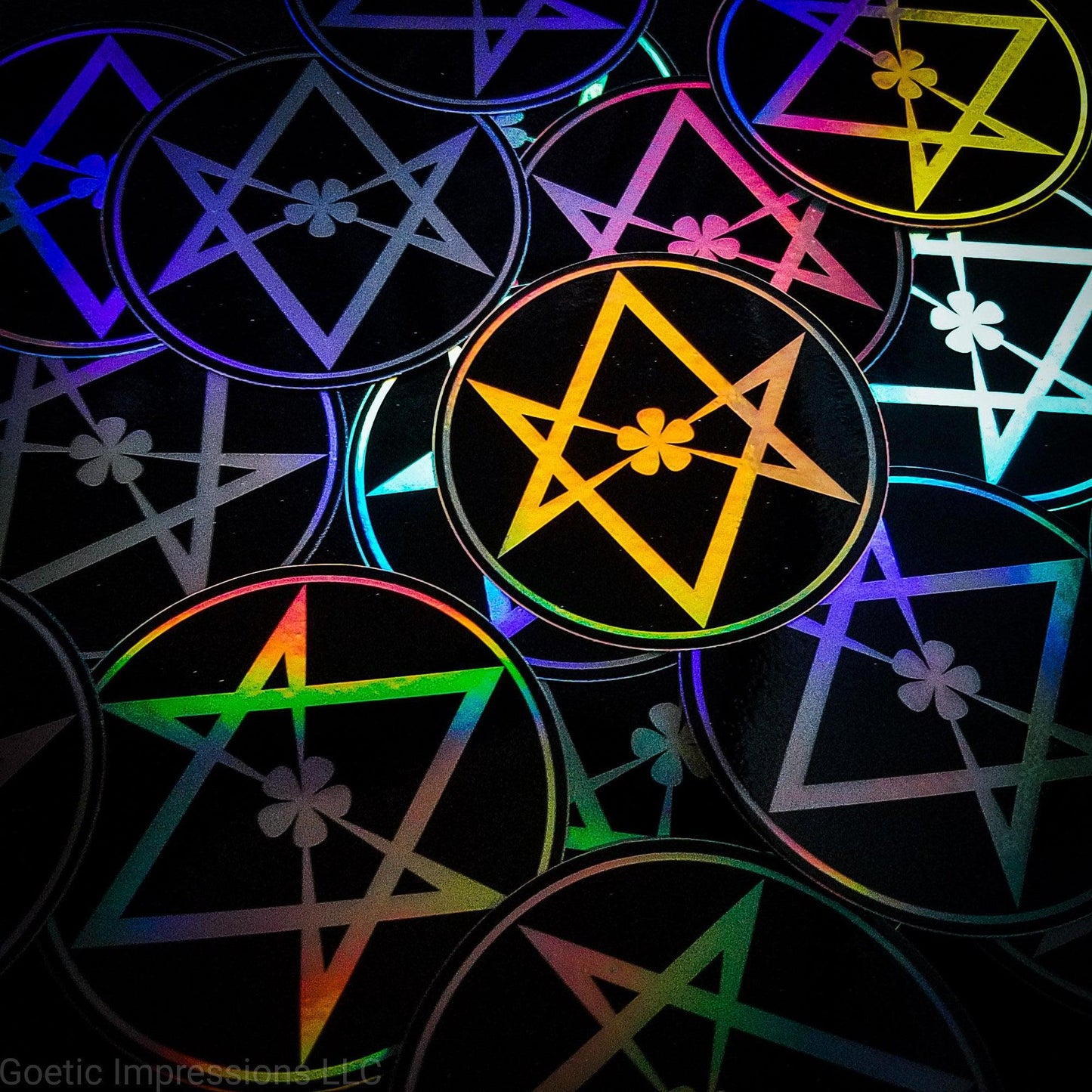 A pile of three inch circular holographic stickers. The stickers have a black background and a white symbol featuring the Unicursal Hexagram with a flower petal in the center. The holographic paper shines in a wide arrange of rainbow colors when the light catches it at different angles.