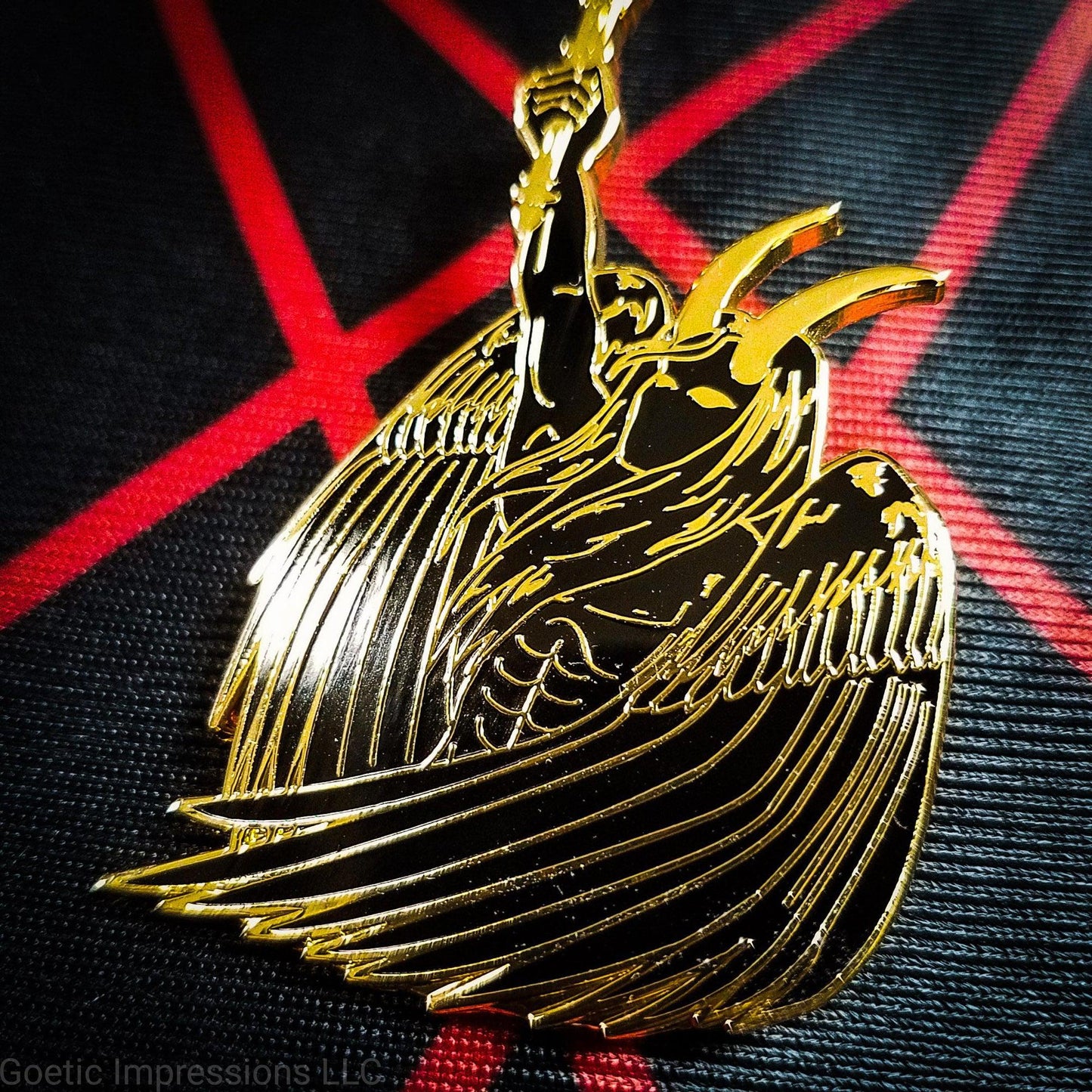 A black and gold hard enamel pin of Lucifer. Lucifer is holding a flaming torch held high and has his wings surrounding him. He has horns and is bare chested. The pin is on a red and black altar cloth with Lucifer's sigil on it.