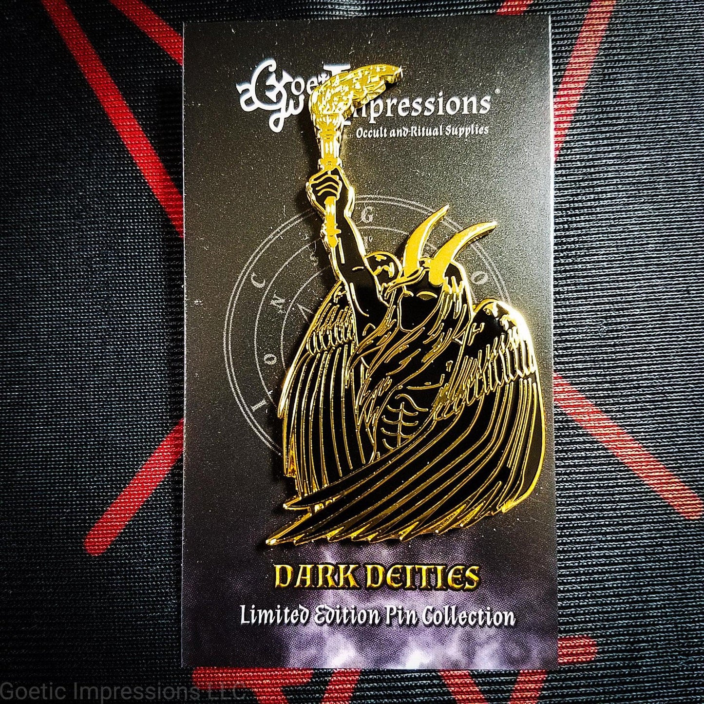A black and gold hard enamel pin of Lucifer. Lucifer is holding a flaming torch held high and has his wings surrounding him. He has horns and is bare chested. The pin is on a Goetic Impressions card back.