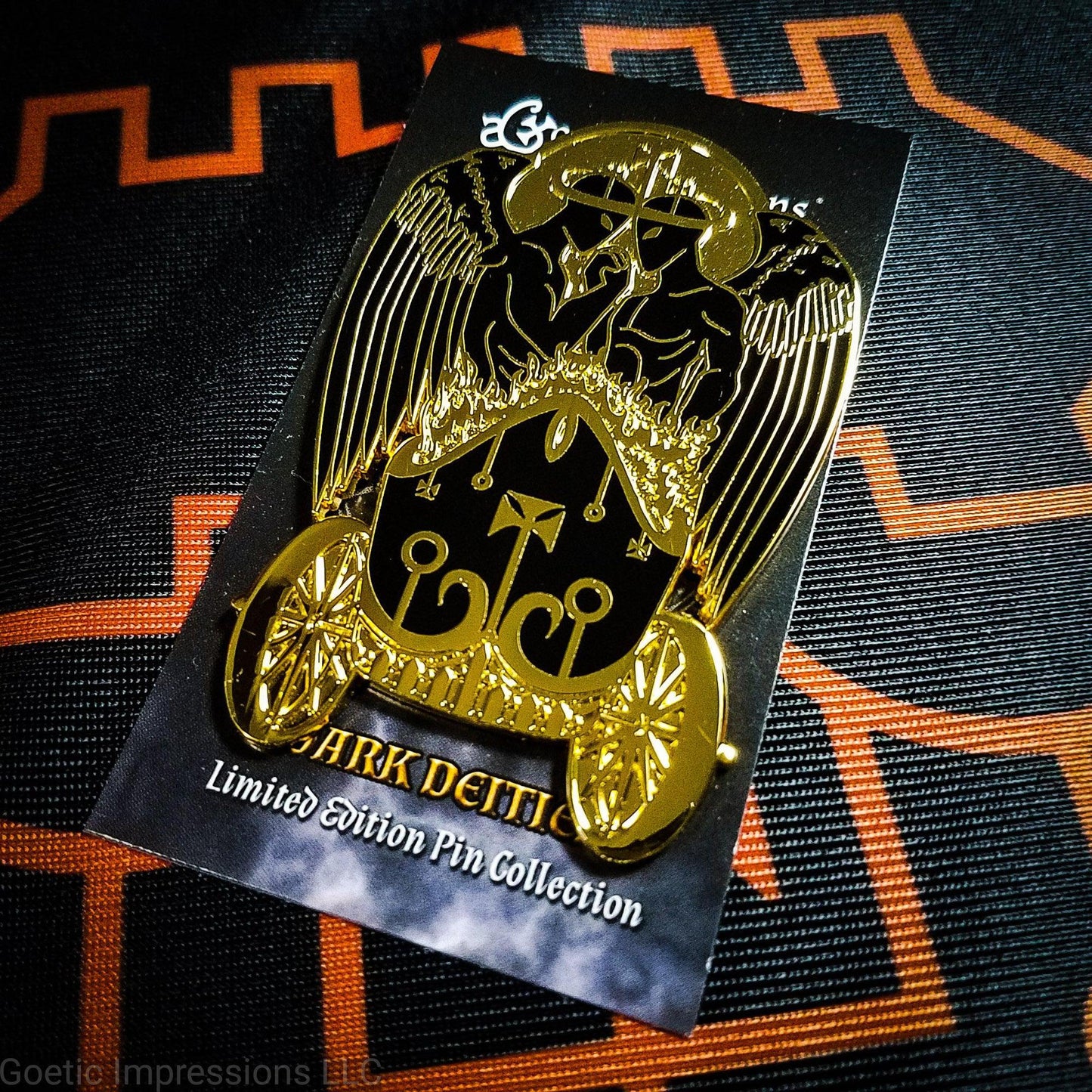Black and gold hard enamel pin featuring the demon Belial. Belial is shown as two angels facing each other with arms interlocked. They are standing in a flaming chariot. The pin is on a black and orange Belial sigil altar cloth. The Belual pin is on a Goetic Impressions card back.