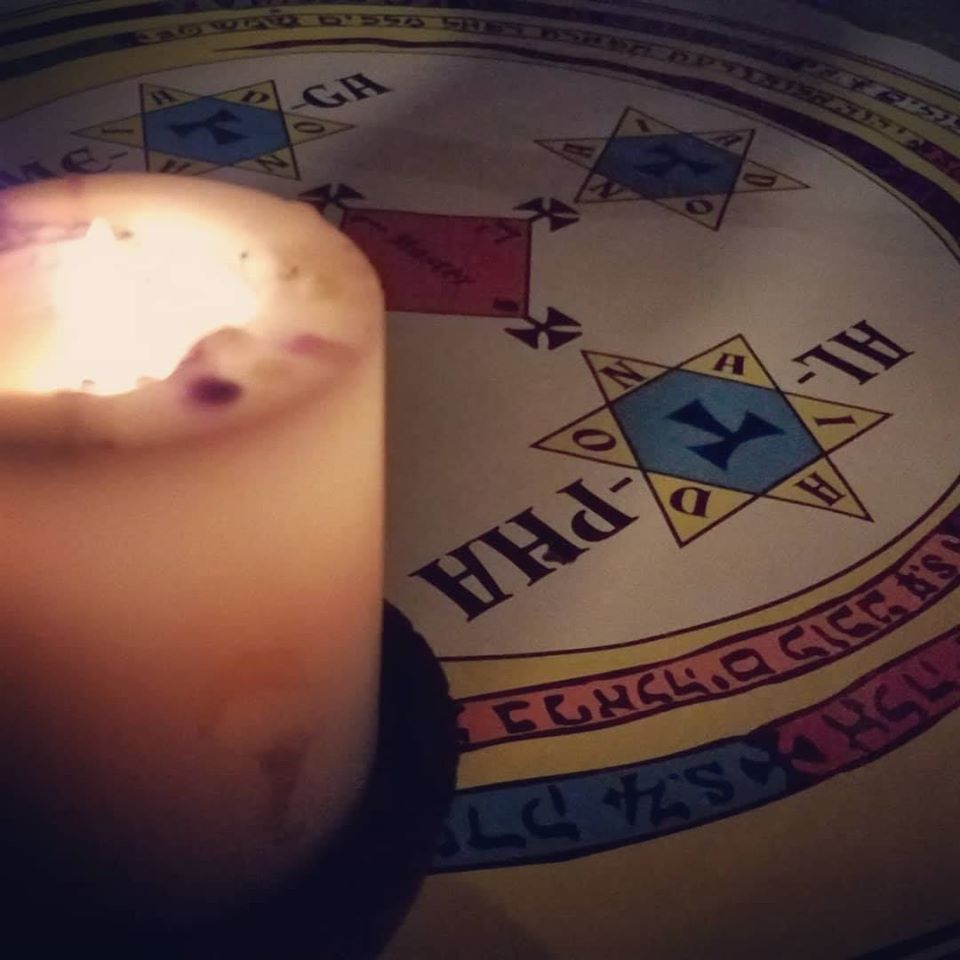 Lesser Key of Solomon Summoning Circle with a candle inthe foreground. The circle is colored with a yellow circle, a spiraling snake of sectioned off colors and a red master square in the center. Around the red square are yellow and blue hexagrams.