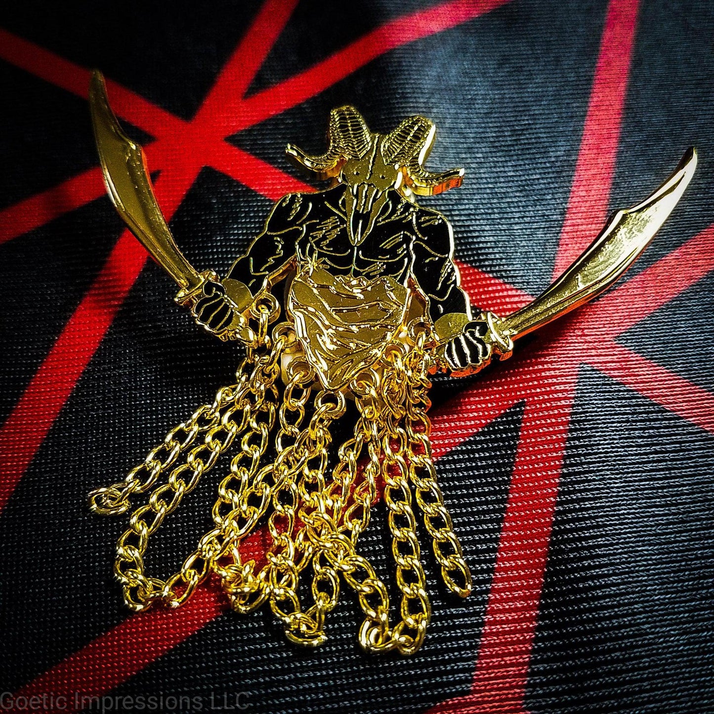 A black and gold hard enamel pin of the demon Azazel. Azazel is shown with the head of a ram skull and human torso brandishing a scimitar in each hand. Azazel is rising up over dunes of a desert.  The pin has chains dangling from it. It is placed on a red and black altar cloth with Azazel's sigil.