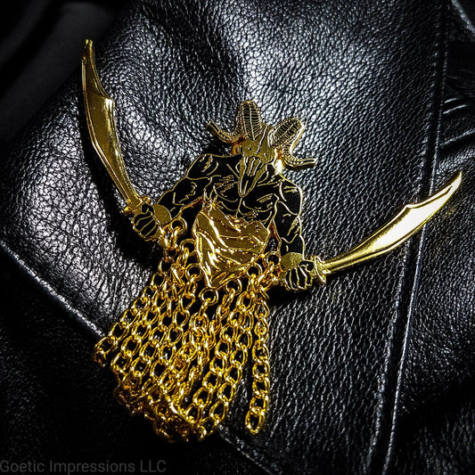 A black and gold hard enamel pin of the demon Azazel. Azazel is shown with the head of a ram skull and human torso brandishing a scimitar in each hand. Azazel is rising up over dunes of a desert.  The pin has chains dangling from it. It is placed on a leather jacket.
