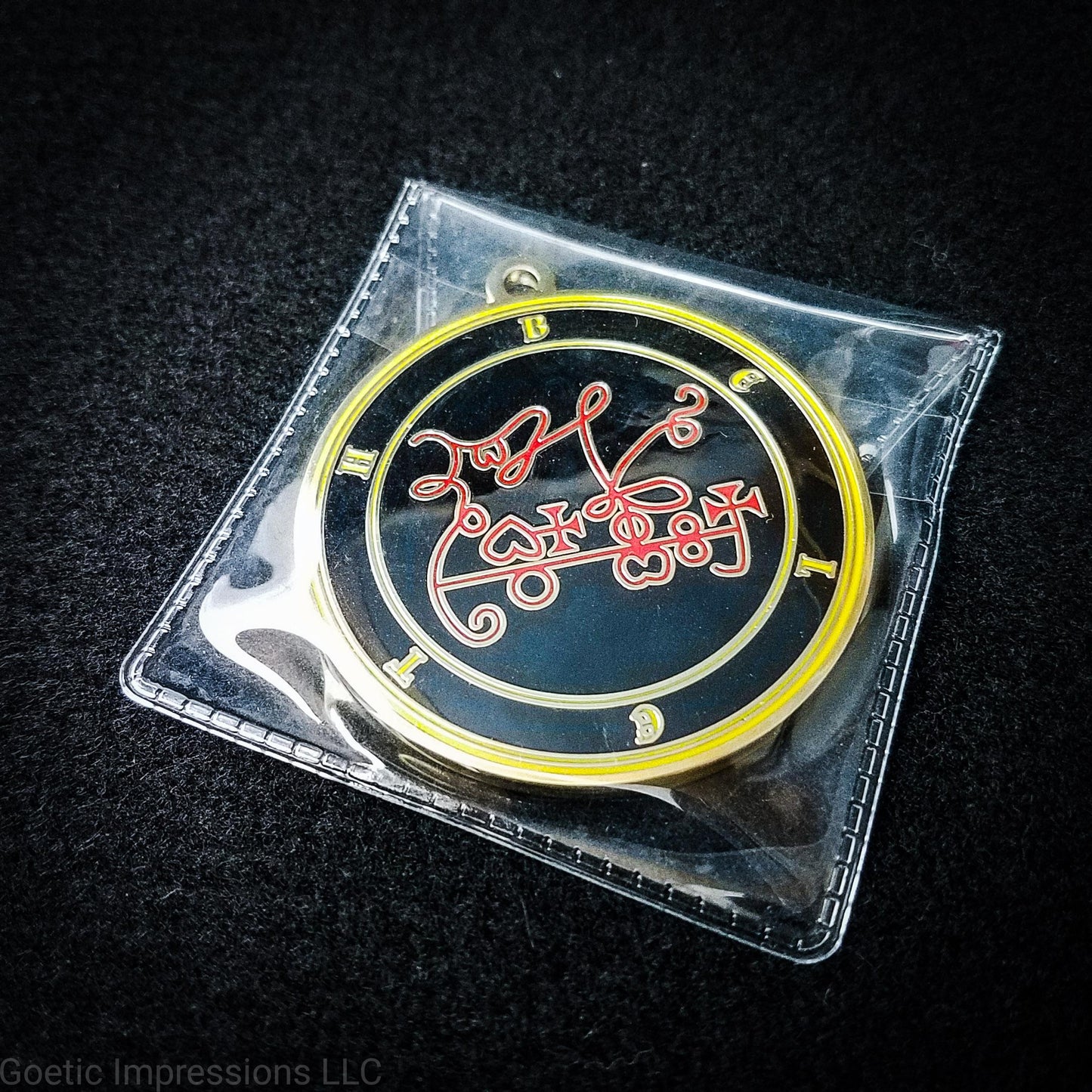 Amulet of Beleth in a PVC pouch. The sigil for Beleth is red. Beleth's name is surrounding the sigil with concentric circles in yellow on a black background. The seal is gold plated.