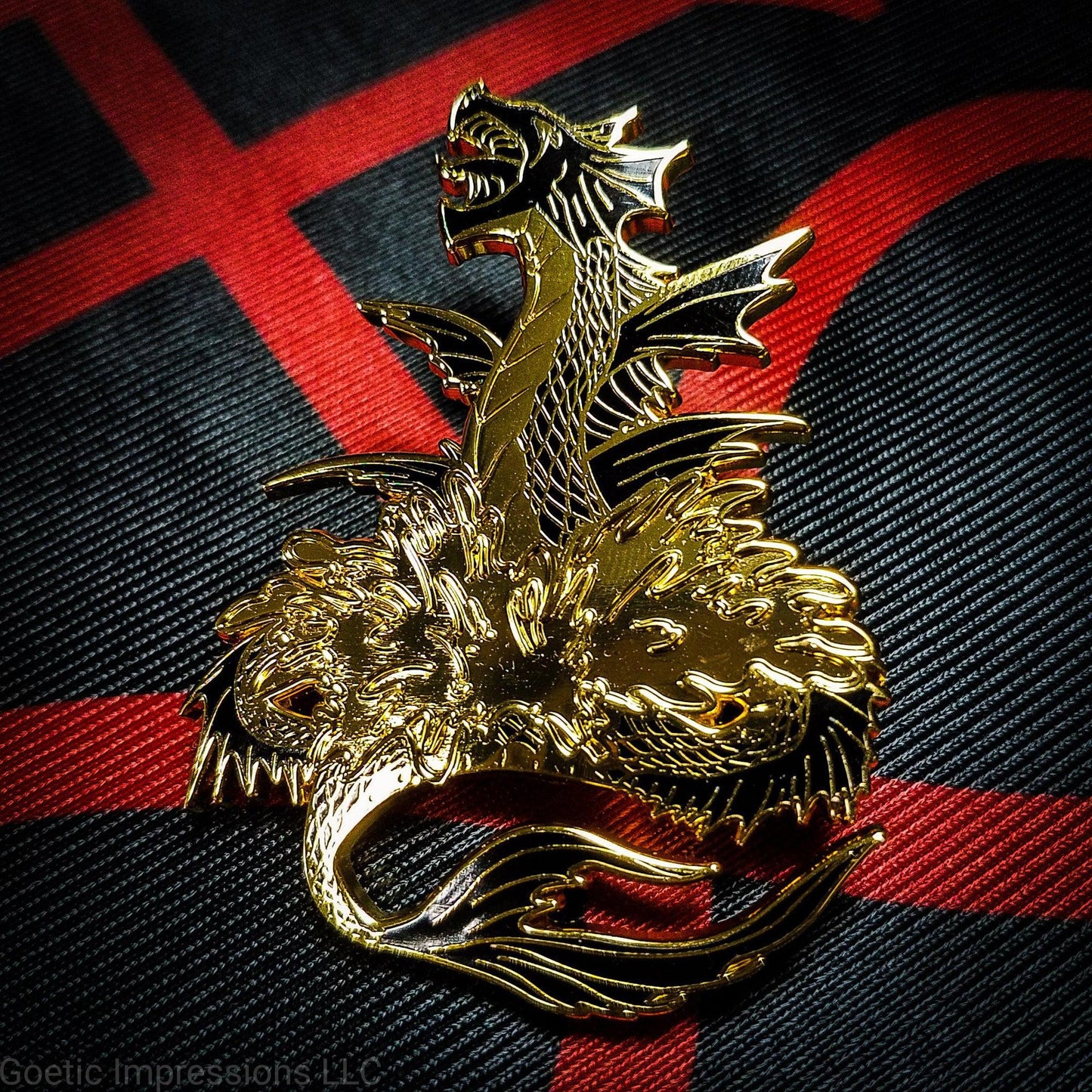 A black and gold hard enamel pin of the sea serpent Leviathan. Leviathan is shown bursting from waters and jaws wide open. The pin is on an altar black and red altar cloth with Levithan's sigil on it.