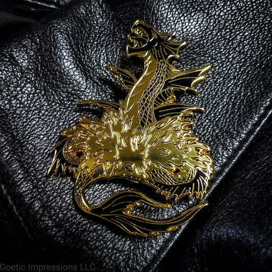 A black and gold hard enamel pin of the sea serpent Leviathan. Leviathan is shown bursting from waters and jaws opened wide. The pin is on a black leather jacket.