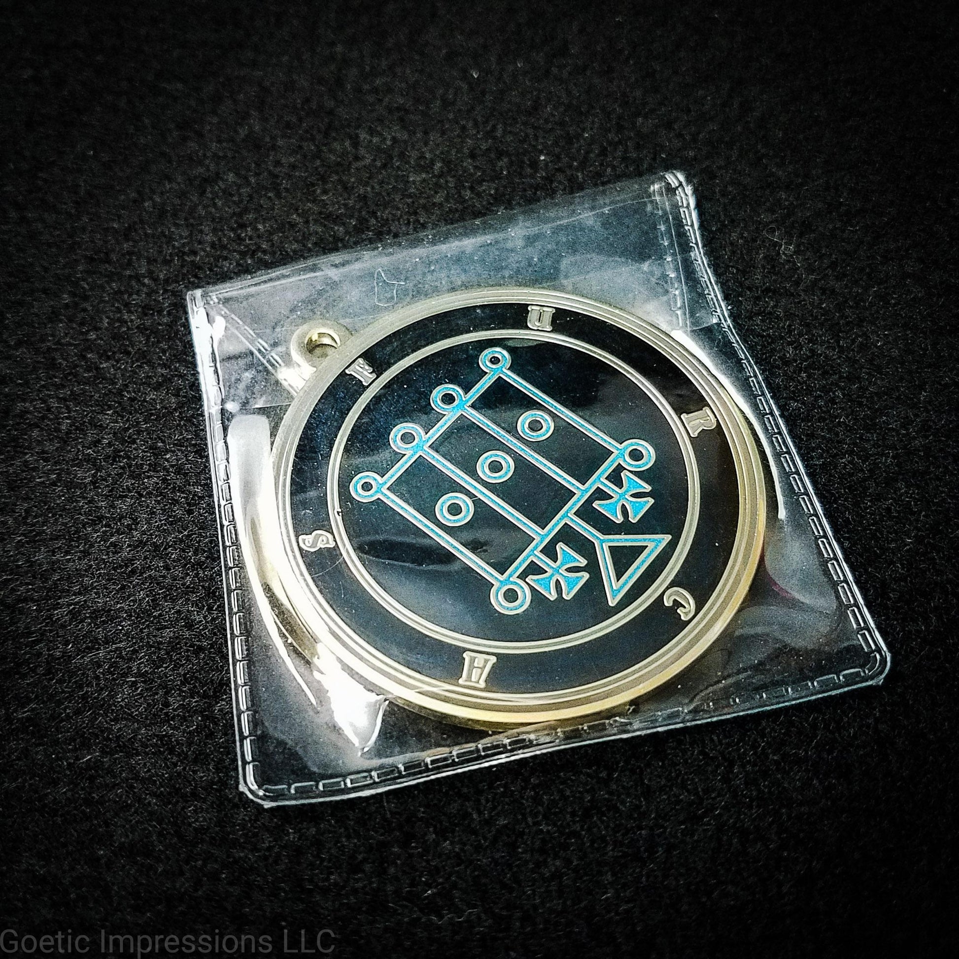 Amulet of Furcas in a PVC pouch. The sigil for Furcas is blue. Furcas' name is surrounding the sigil with concentric circles in gray on a black background. The seal is brass plated.