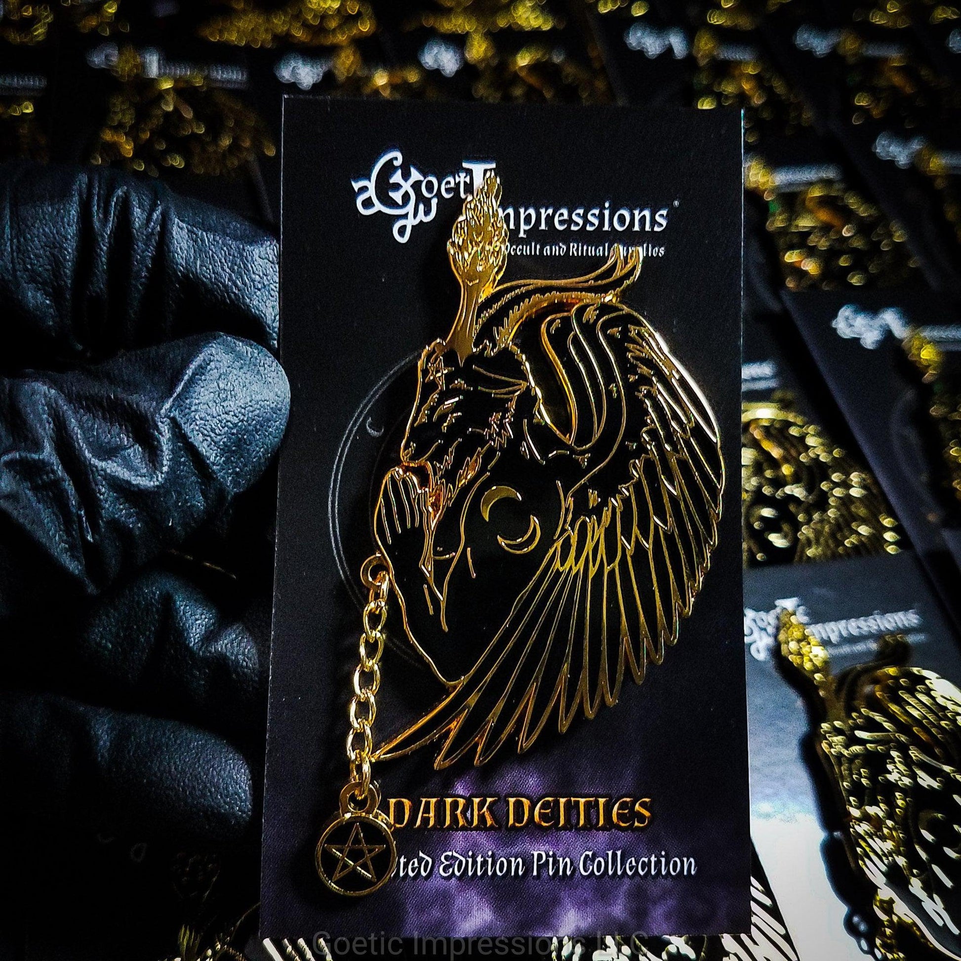 A black and gold hard enamel pin featuring Baphomet in a side profile praying pose. There is a pentacle chain rosary in Baphomet's hands. The pin is shown on a Goetic Impressions backing card held by a glove hand.