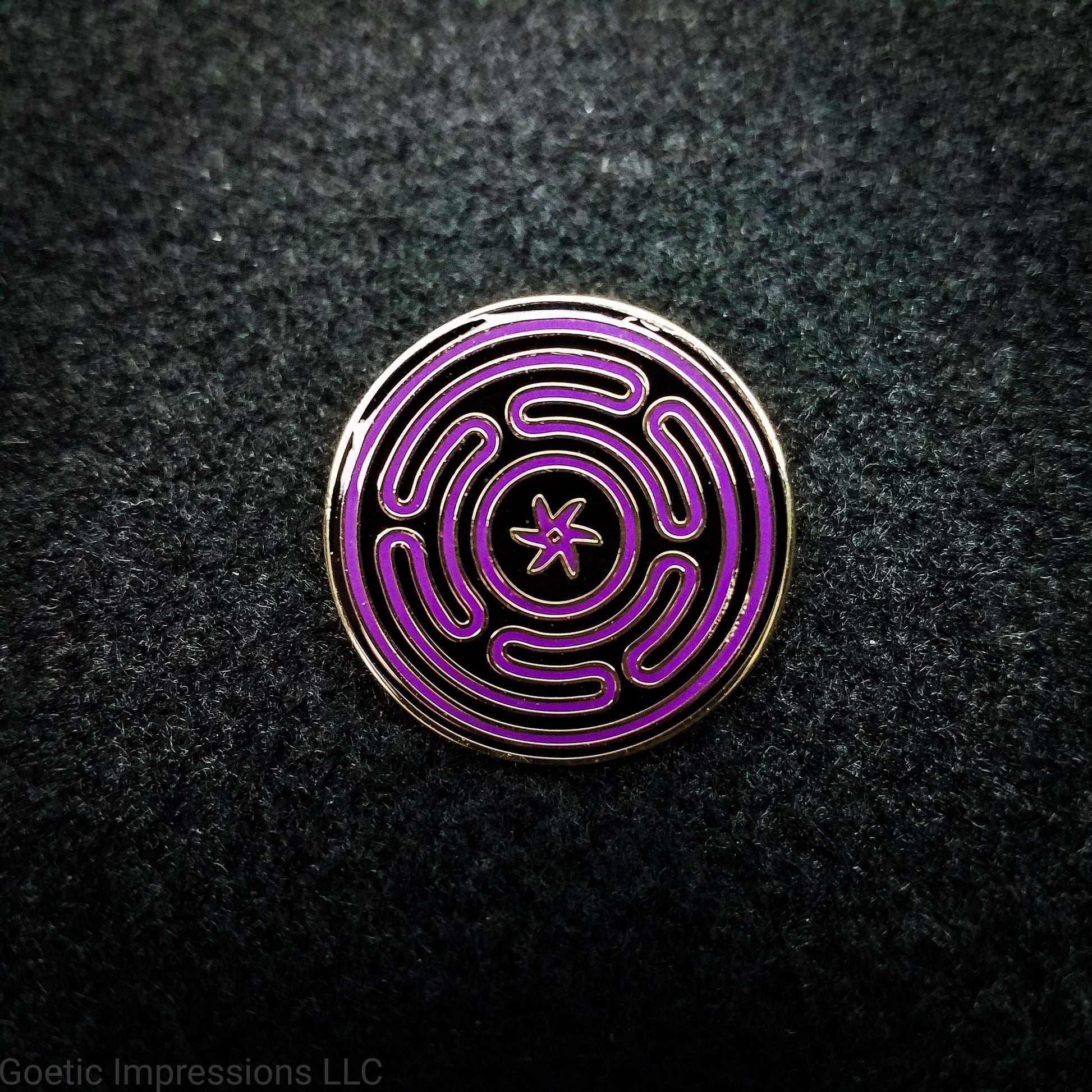 Wheel of Hecate sigil pin that is gold plated. The sigil is purple on a black background.