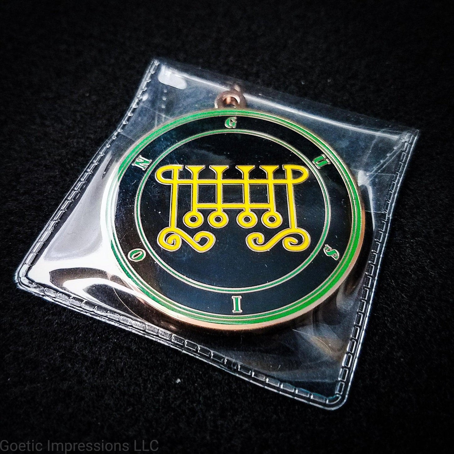 Amulet of Gusion in a PVC pouch. The sigil for Gusion is yellow. Gusion's name is surrounding the sigil with concentric circles in green on a black background. The seal is copper plated.