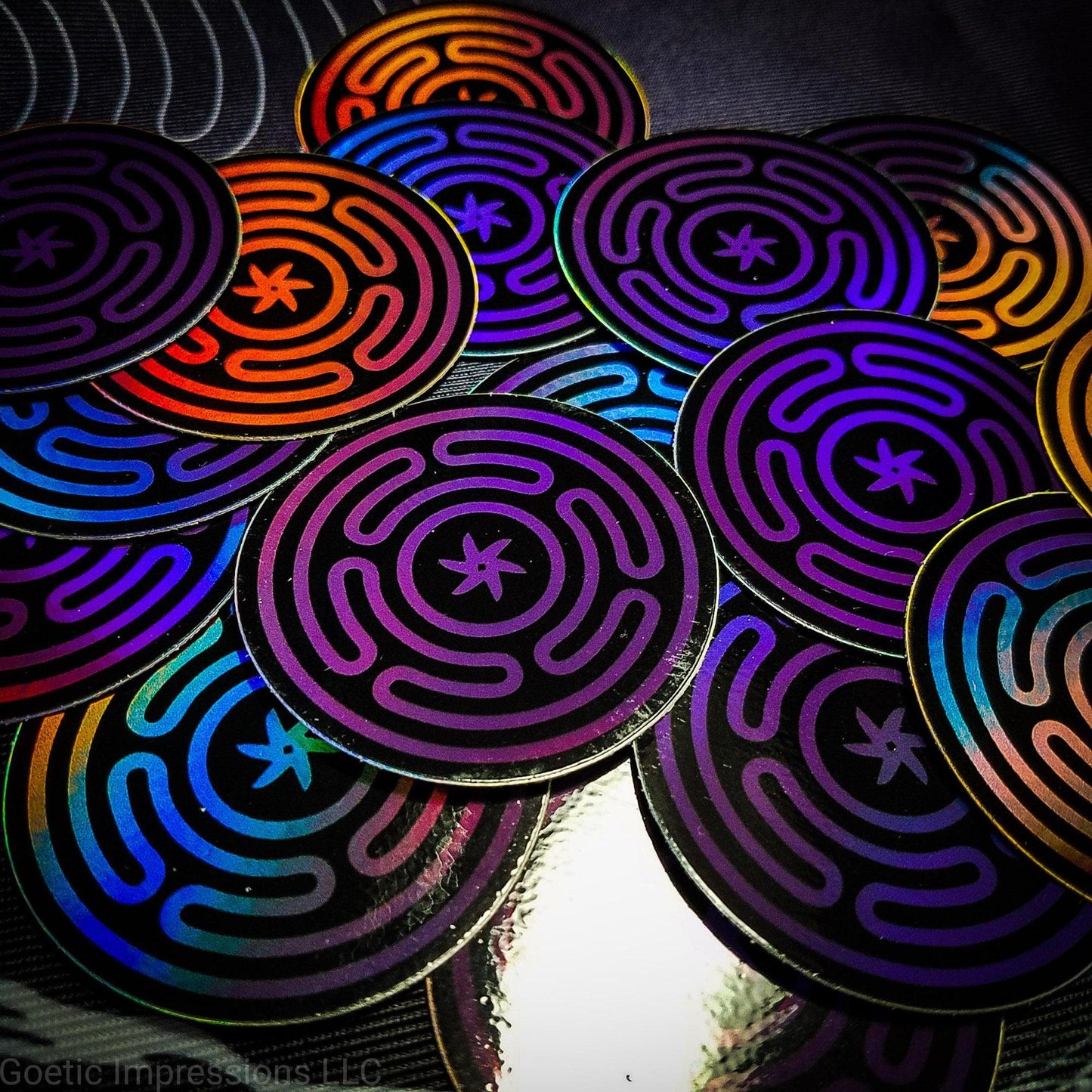 A pile of Holographic stickers featuring the wheel of Hecate or Stropholos. The base color of the sigil is purple on a black background.