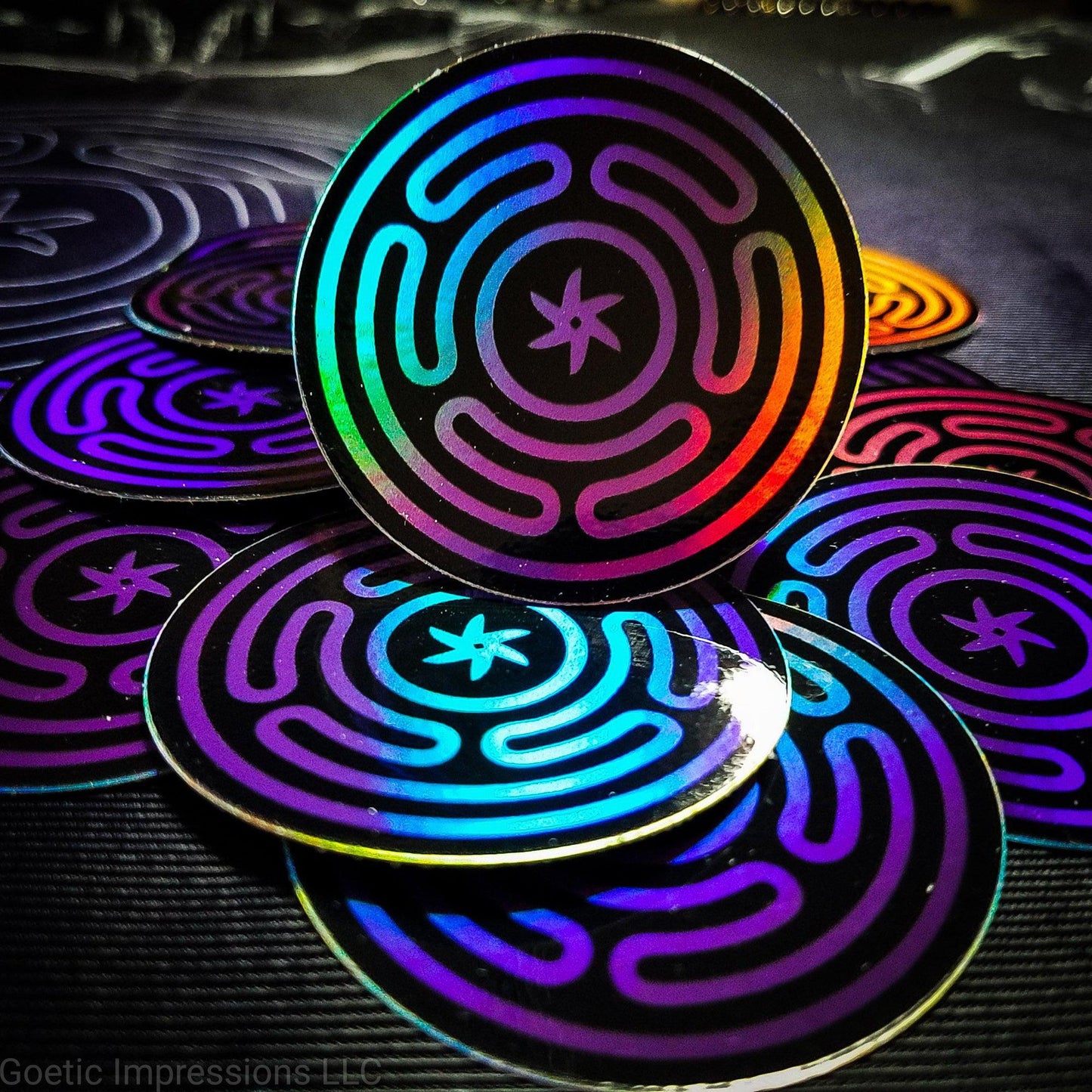 A pile of Holographic stickers featuring the wheel of Hecate or Stropholos. The base color of the sigil is purple on a black background.