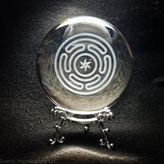 A crystal ball with the engraved sigil of Hecate in the center. The ball sits on a silver stand. This sigil is also called the Stropholos or Wheel of Hecate.