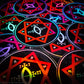 A pile of three inch circular holographic stickers. The stickers have a black background and a white  and red symbol featuring the Star of Babalon. The holographic paper shines in a wide arrange of rainbow colors when the light catches it at different angles. 