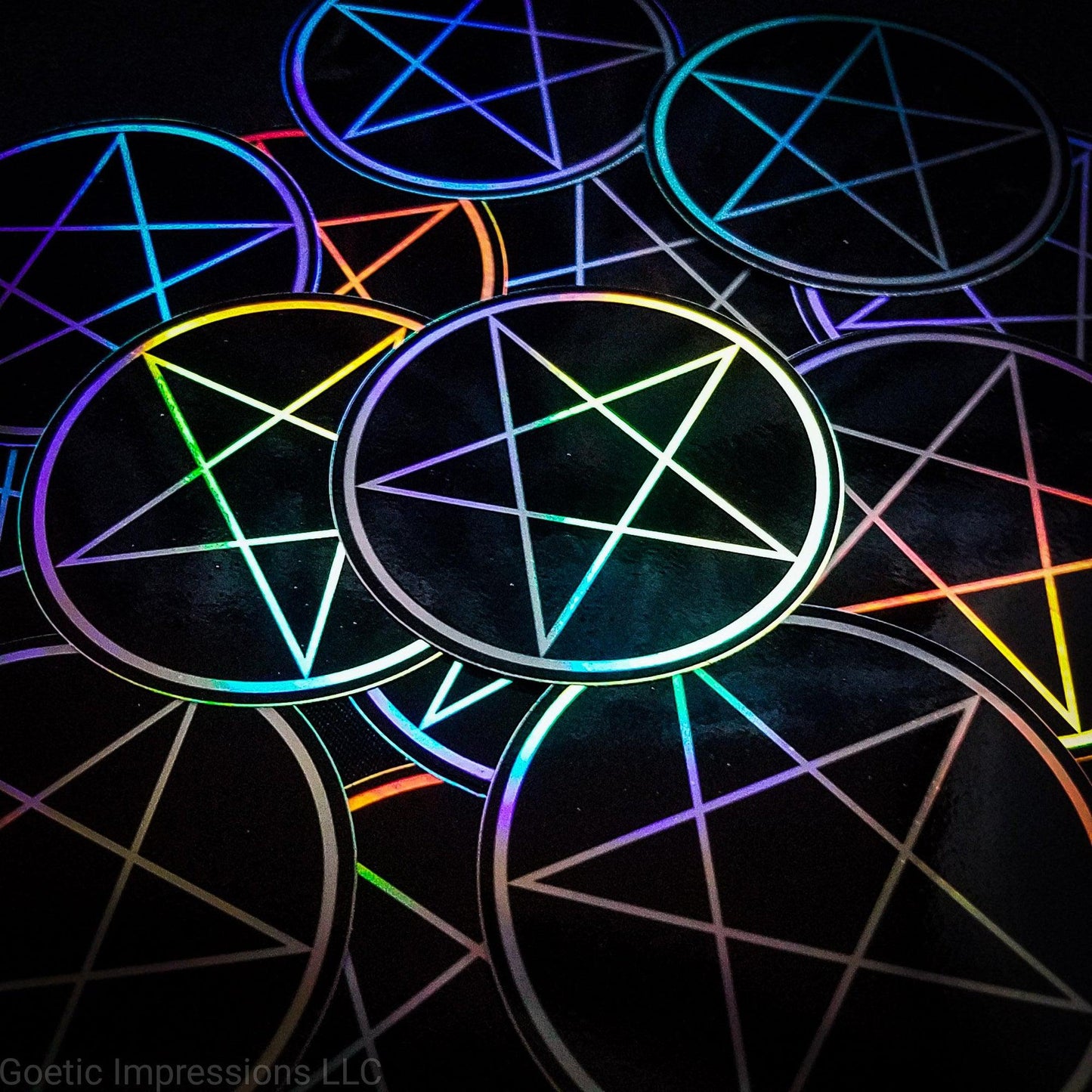 A pile of three inch circular holographic stickers. The stickers have a black background and a white symbol featuring the a traditional pentacle. The holographic paper shines in a wide arrange of rainbow colors when the light catches it at different angles. 