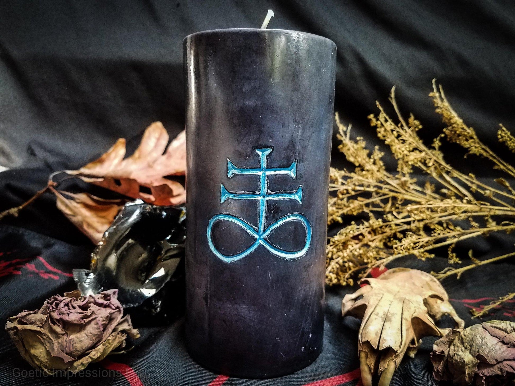 Black pillar candle with blue Leviathan cross carved into it.