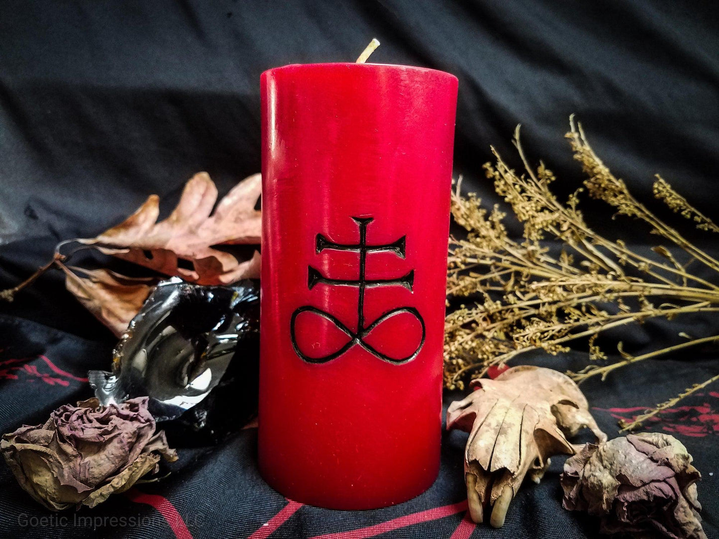 Red pillar candle with a black Leviathan cross carved into it.