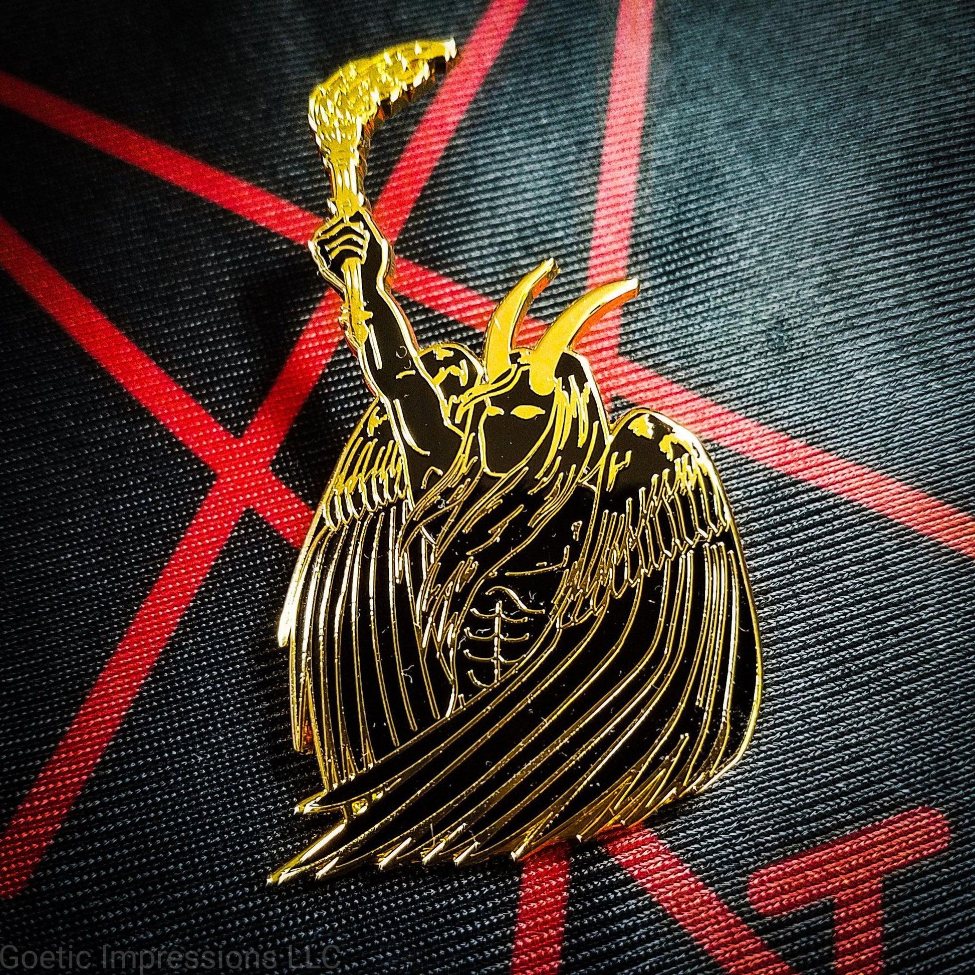 A black and gold hard enamel pin of Lucifer. Lucifer is holding a flaming torch held high and has his wings surrounding him. He has horns and is bare chested. The pin is on a red and black altar cloth with Lucifer's sigil on it. 