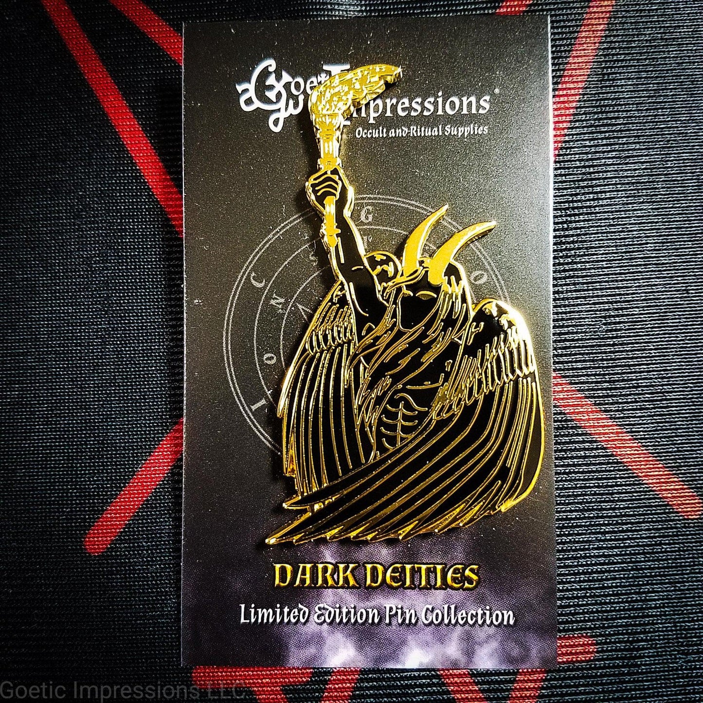 A black and gold hard enamel pin of Lucifer. Lucifer is holding a flaming torch held high and has his wings surrounding him. He has horns and is bare chested. The pin is on a Goetic Impressions card back. 