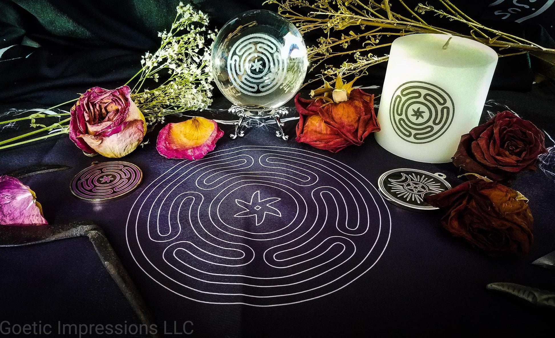 An altar with vrarious ritual tools featuring the Stropholos or Wheel of Hecate. The sigil is printed on a black and purple altar cloth. On the cloth is a white candle, a crystal ball and a gold medallion featuring the sigil. Roses and other dried herbs are decorated around the altar.