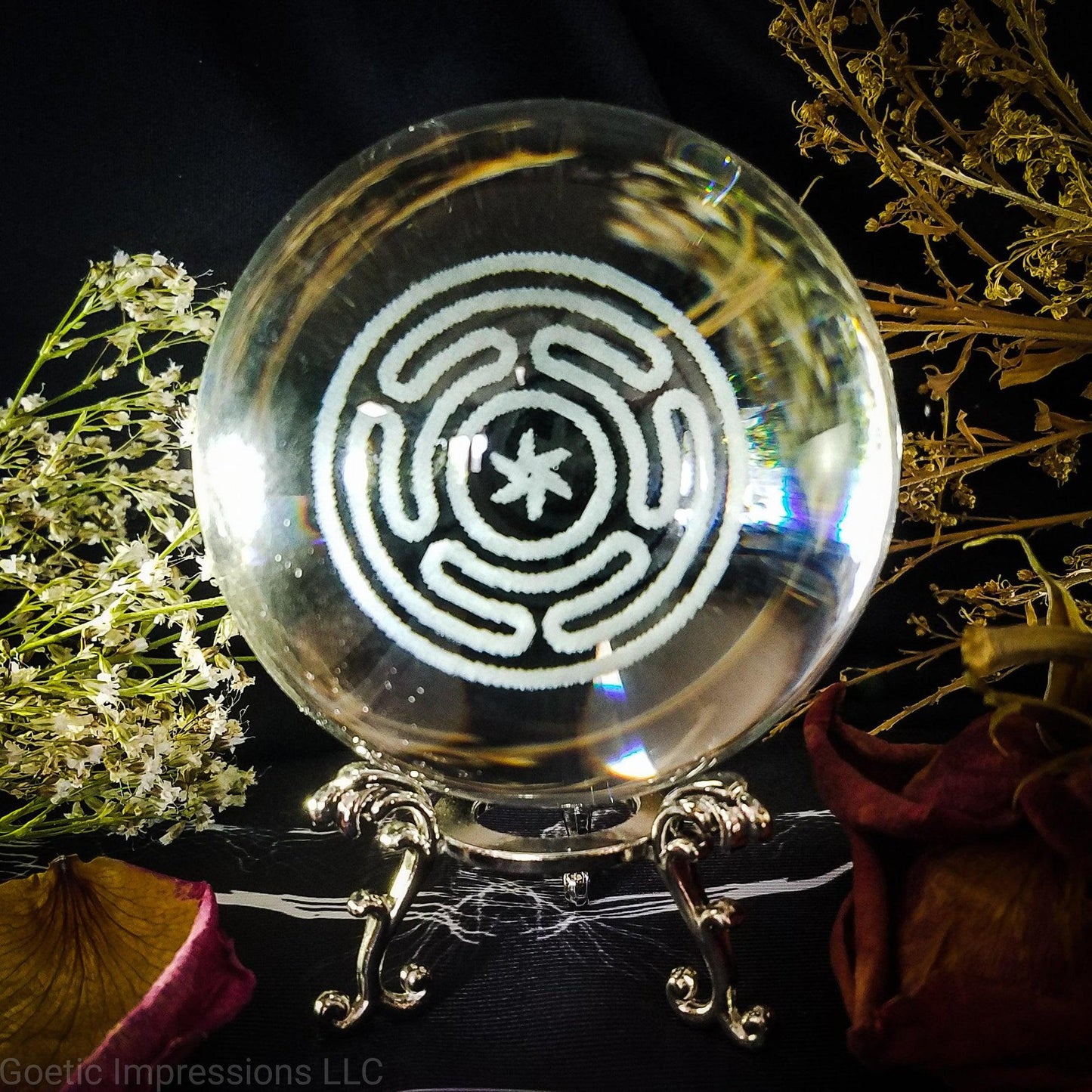 A crystal ball with the engraved sigil of Hecate in the center. The ball sits on a silver stand. This sigil is also called the Stropholos or Wheel of Hecate.