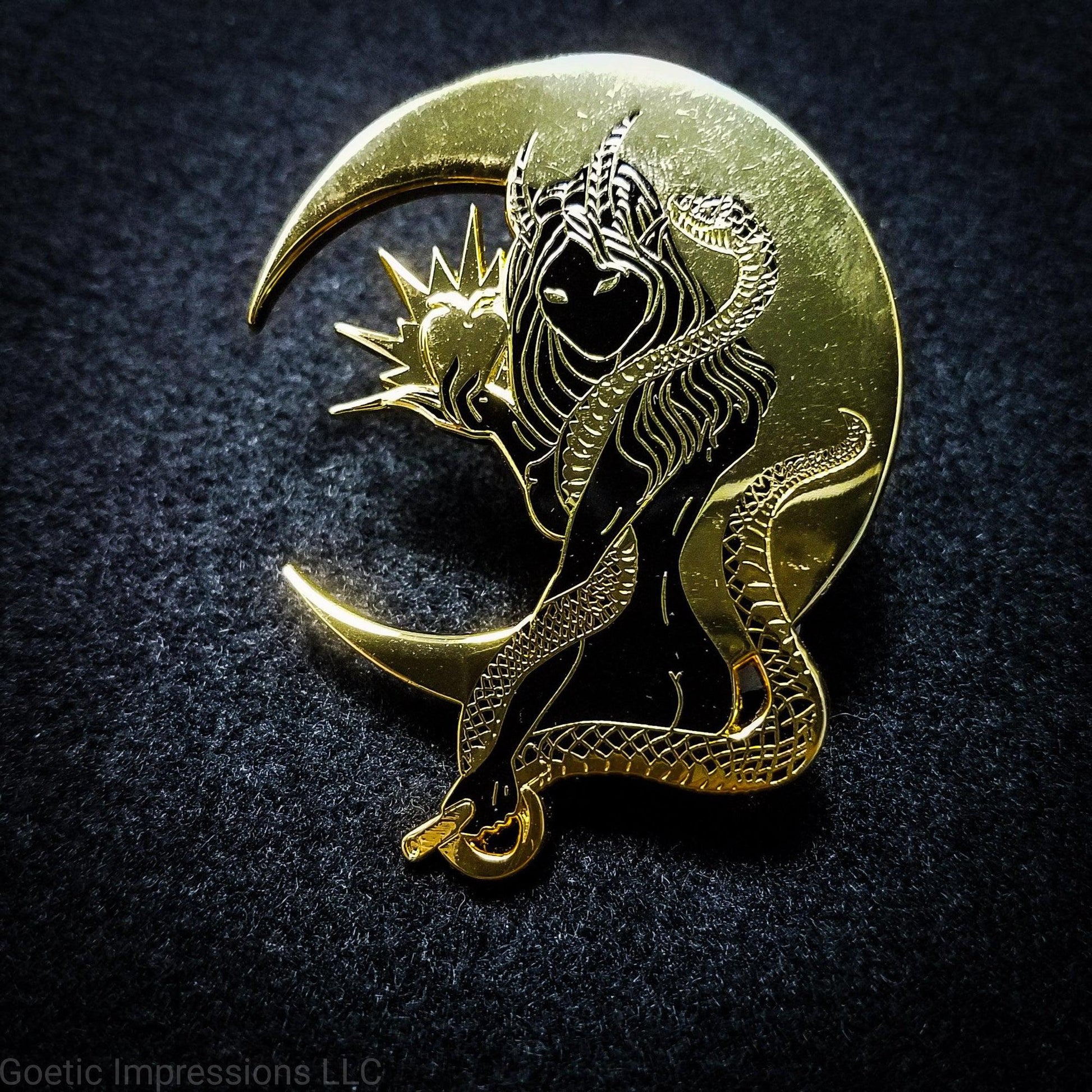 A black and gold hard enamel pin of Lilith. Lilith is holding a shining apple in one hand and a rod and circle in the other. Her one arm is coiled with a serpent. A cresent moon is behind her.