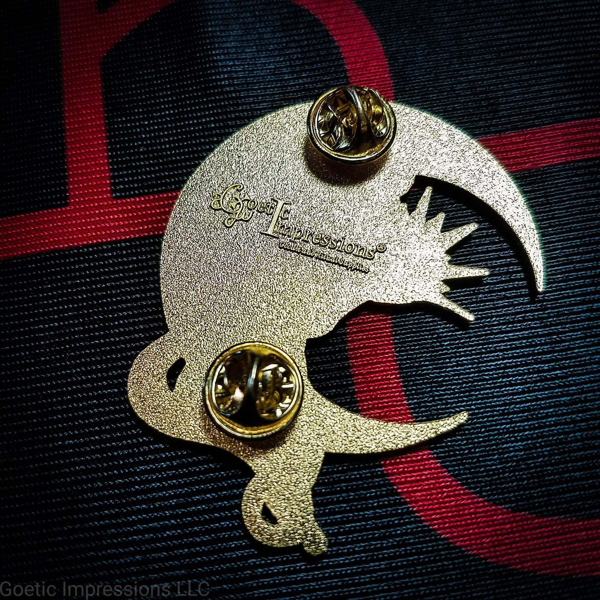 The back of a Lilith pin with the Goetic Impressions logo stamped on the back. The pin has two clutches.