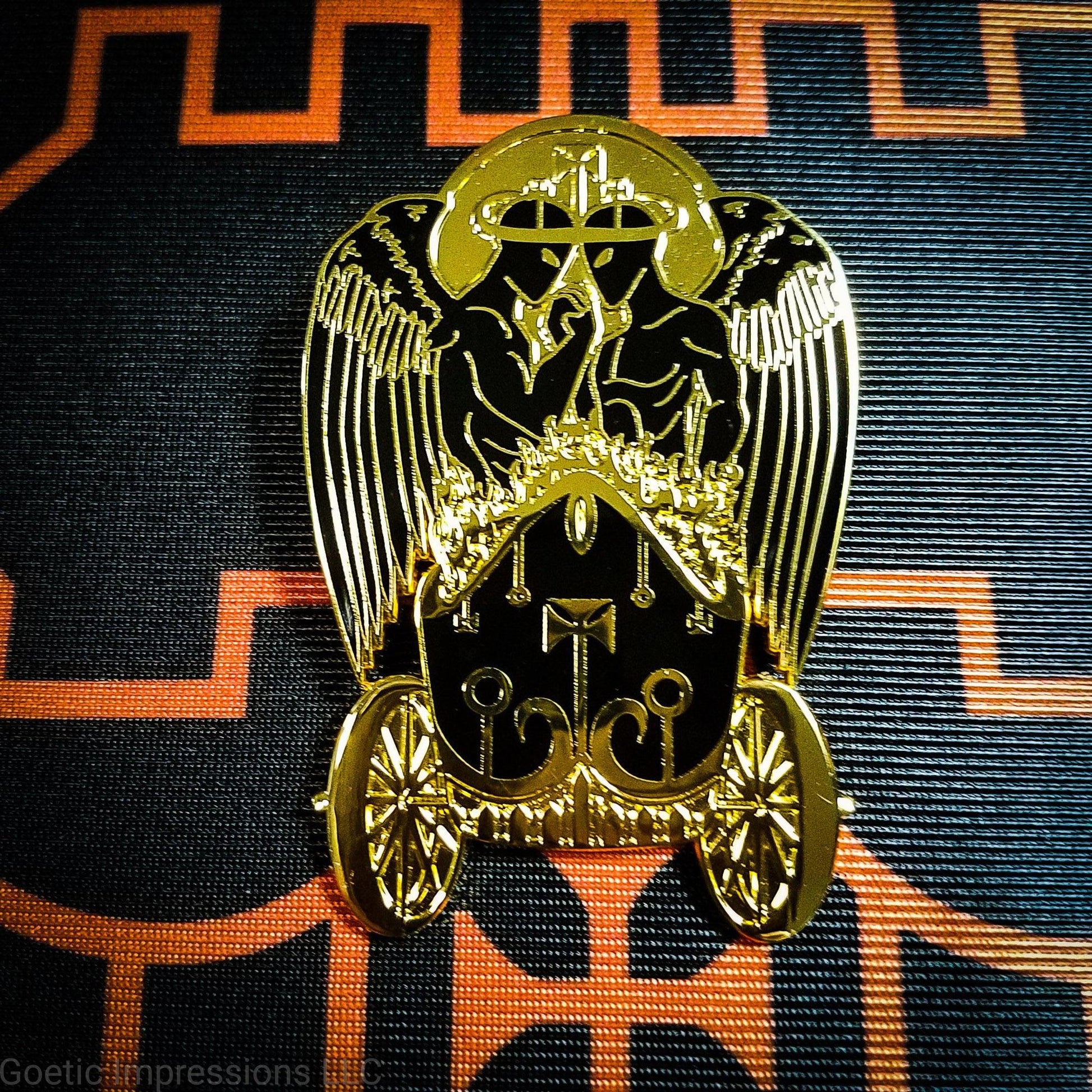 Black and gold hard enamel pin featuring the demon Belial. Belial is shown as two angels facing each other with arms interlocked.  They are standing in a flaming chariot.  The pin is on a black and orange Belial sigil altar cloth. 