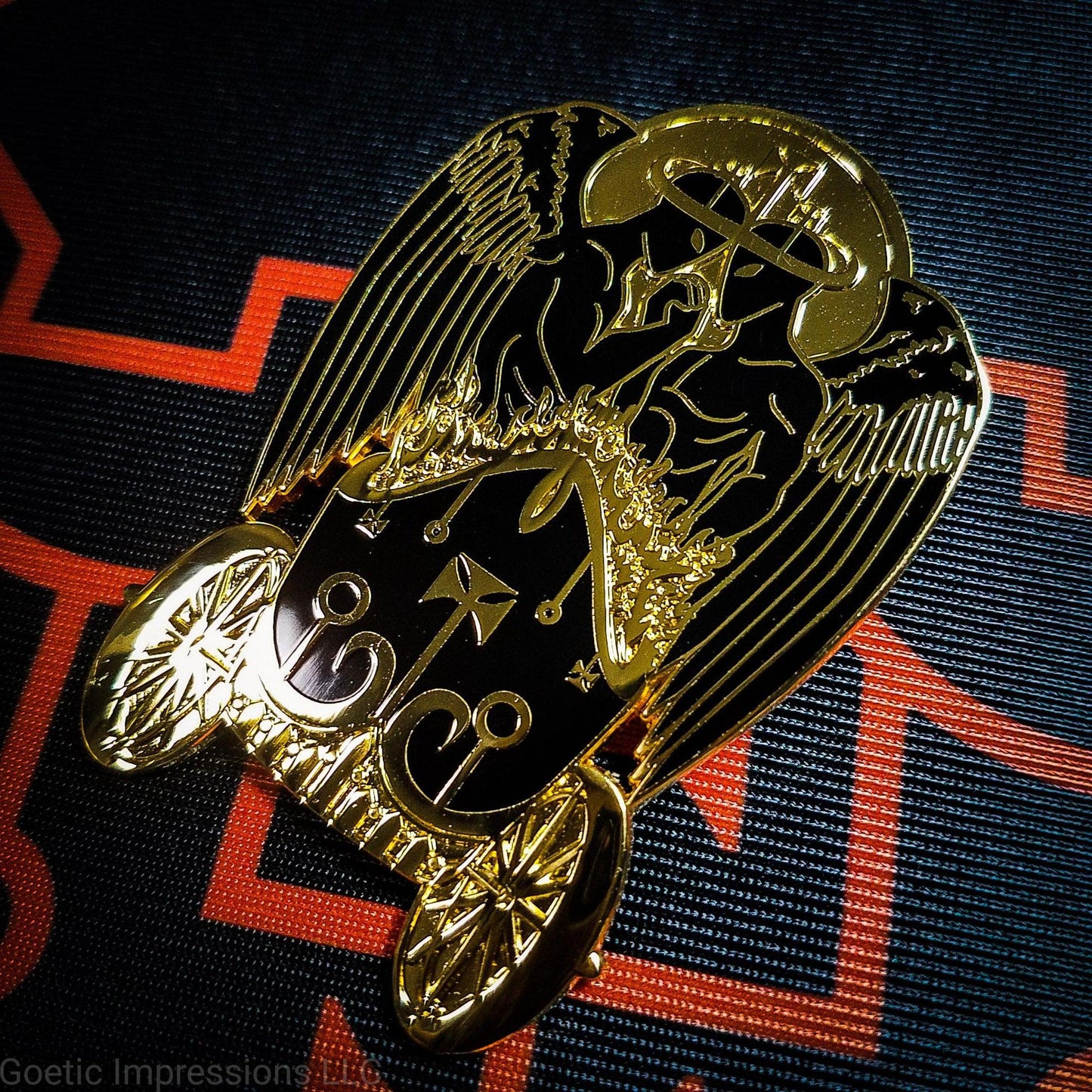 Black and gold hard enamel pin featuring the demon Belial. Belial is shown as two angels facing each other with arms interlocked.  They are standing in a flaming chariot.  The pin is on a black and orange Belial sigil altar cloth. 