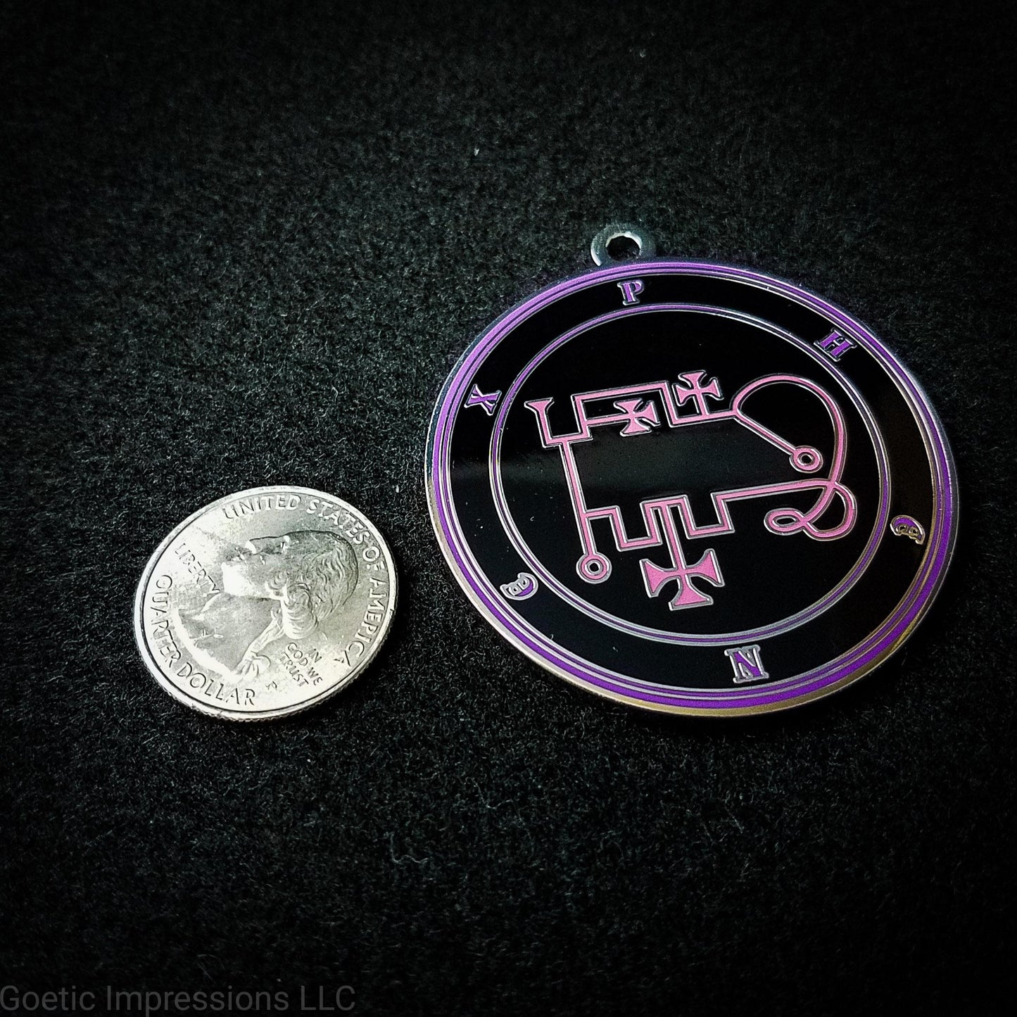 Seal of Phenex next to a quarter. The seal medallion measures two inches in diameter. The sigil is pink with purple letters and circles on a black background. 