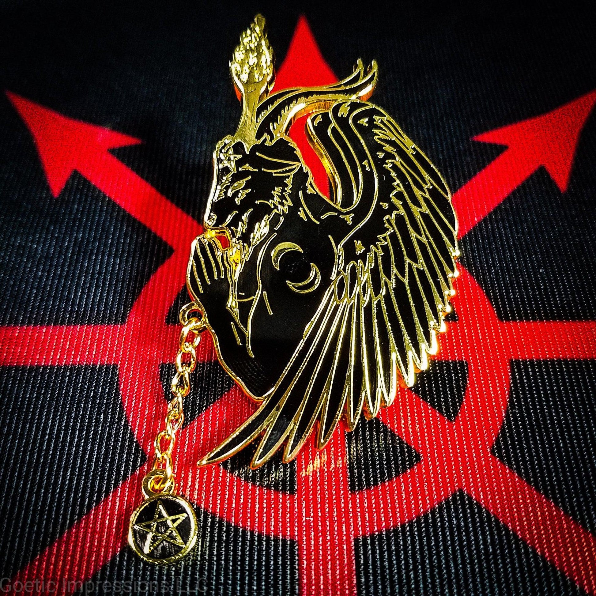 A black and gold hard enamel pin featuring Baphomet in a side profile praying pose. There is a pentacle chain rosary in Baphomet's hands. The pin is on a black and red altar cloth with the chaos star in the center. 
