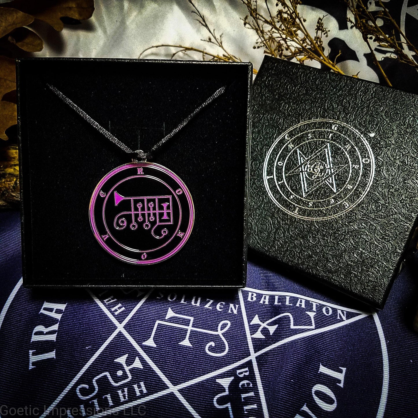Necklace of Ronove in a Goetic Impressions gift box stamped in silver foil. The sigil for Ronove is purple. Ronove's name is surrounding the sigil with concentric circles in purple on a black background. The seal is silver plated. The box is on a purple altar cloth with the Tetragrammaton in white.