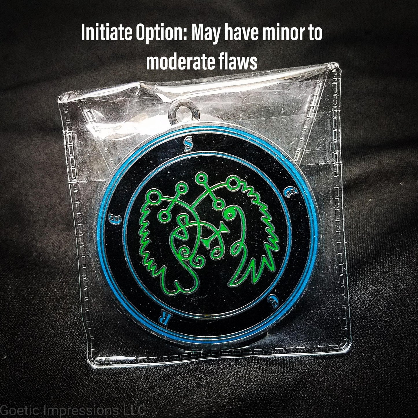 Amulet of Seere in a PVC pouch. The sigil for Seere is green. Seere's name is surrounding the sigil with concentric circles in blue on a black background.  The seal is silver plated.
