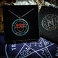A Sitri medallion in a Goetic Impressions gift box. The medallion has a satin cord necklace. The sigil on the talisman is red with blue circles and text. The gift box is on a pentacle of solomon altar cloth.