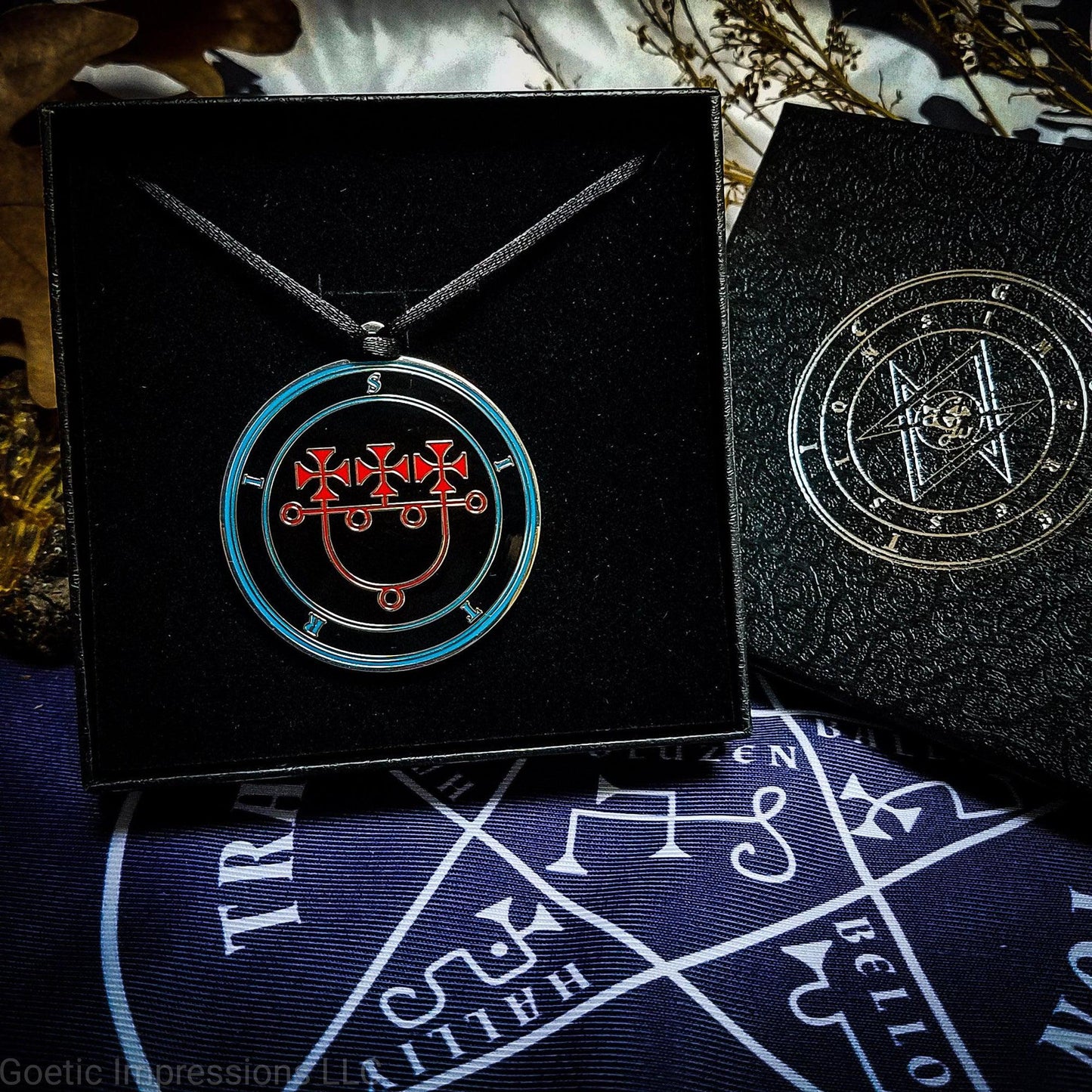 A Sitri medallion in a Goetic Impressions gift box. The medallion has a satin cord necklace. The sigil on the talisman is red with blue circles and text. The gift box is on a pentacle of solomon altar cloth.