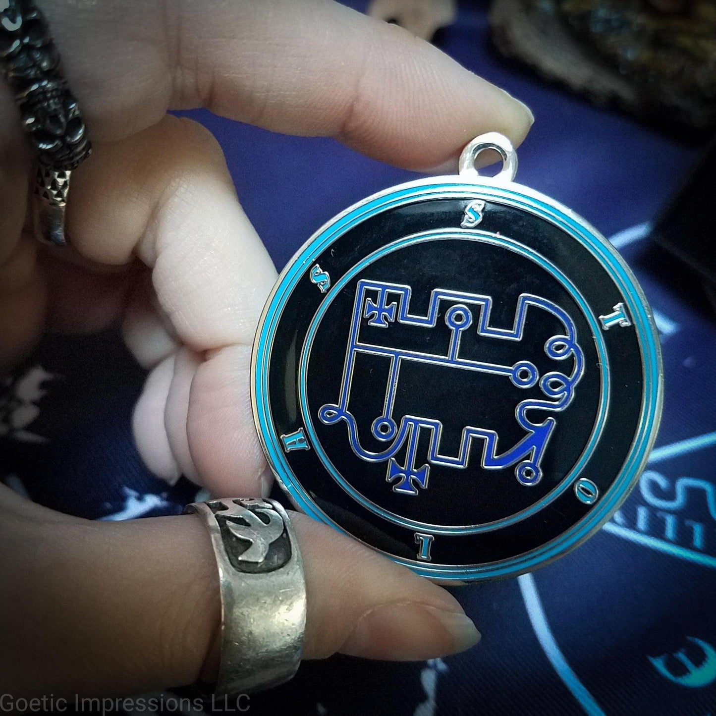 Hand holding a talisman of goetic spirit Stolas . Stolas's sigil is dark blue with the circles surrounding in teal along with the name on a black background. 